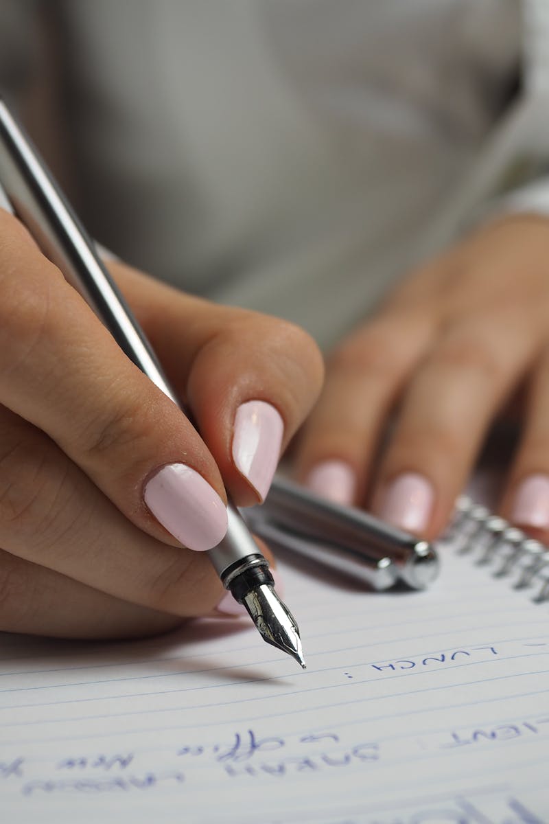 Woman in White Long Sleeved Shirt Holding a Pen Writing on a Paper